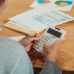 Person using a calculator with financial papers on a desk.